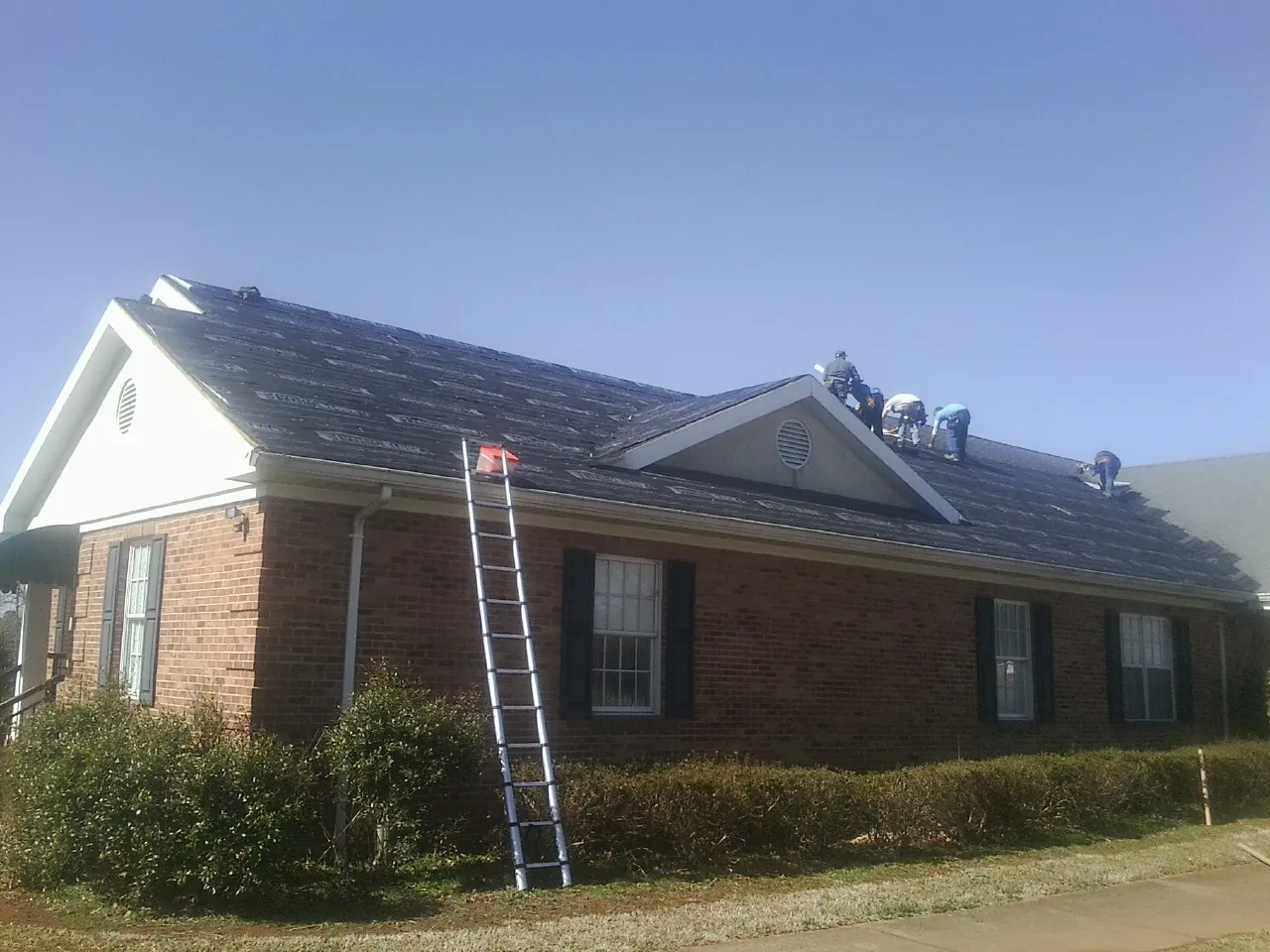 Crew tearing shingles off a brick ranch roof with a ladder set — Metal Roof Repair work by our crew in Weir