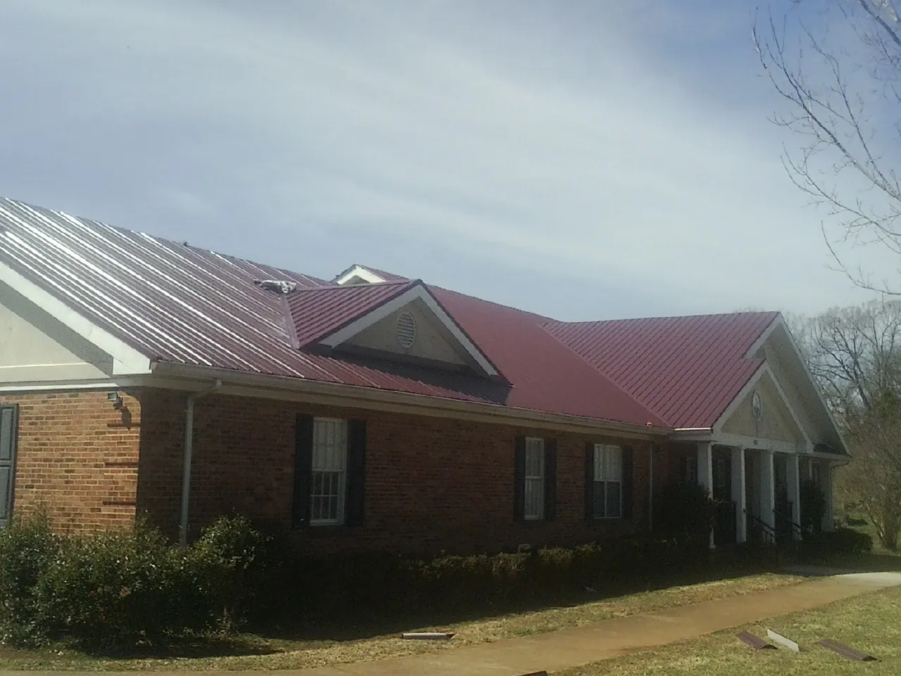 Red metal roof with gabled entries on a long brick building, from a Hail Damage Roof Repair job in Weir